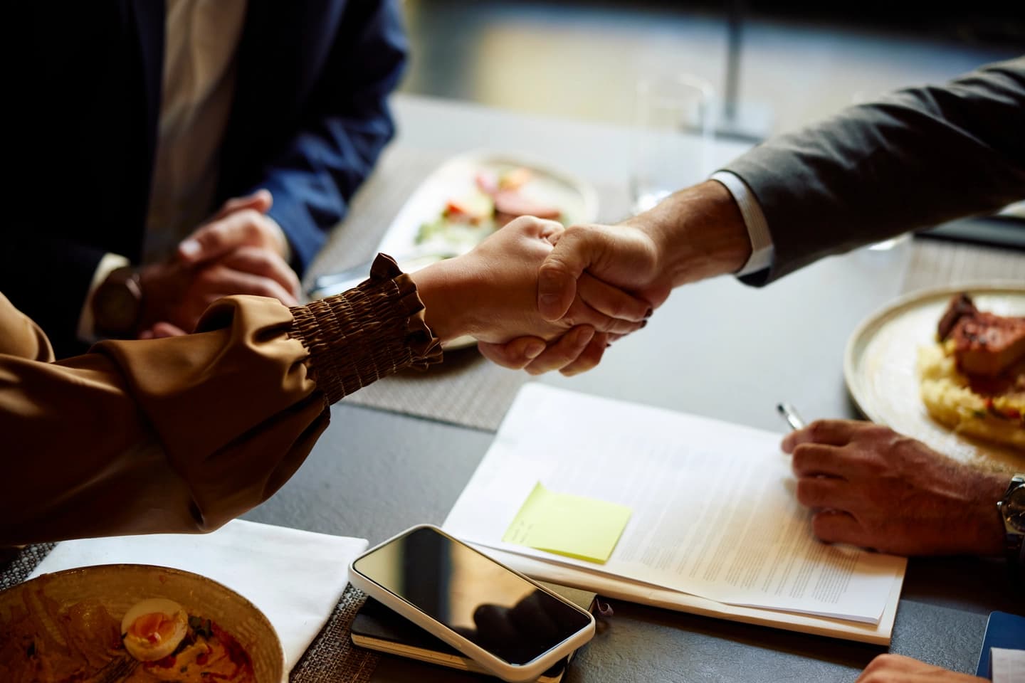 Business partners shaking hands over a restaurant table